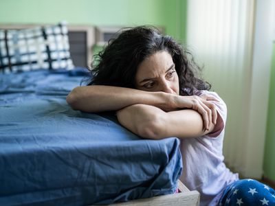 Worried woman sitting on floor next to bed