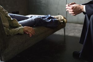 Young woman lying on couch and therapist leaning toward her with hands clasped