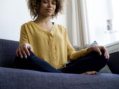 Young woman sitting on couch at home meditating